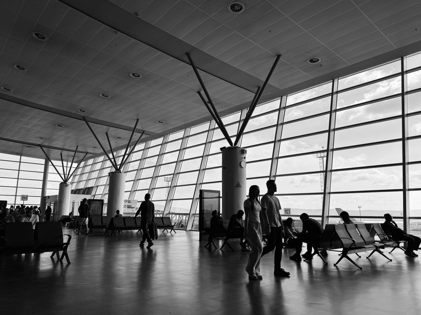 Planejamento de Viagens. — Black and white view of a busy airport terminal with travelers waiting and walking.