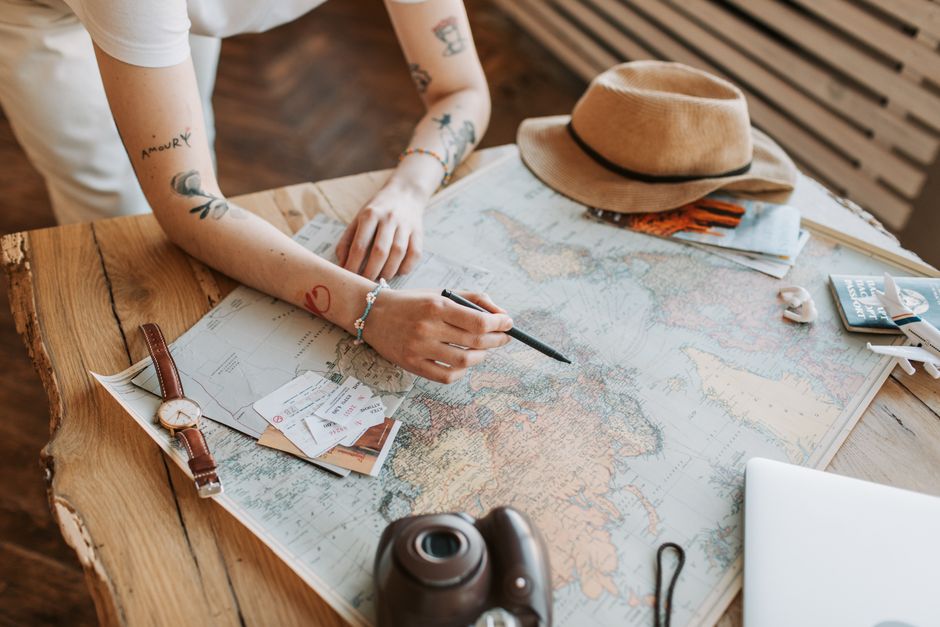 Planejamento de Viagens. — Tattooed woman planning a trip with a world map, passports, and travel essentials on a wooden